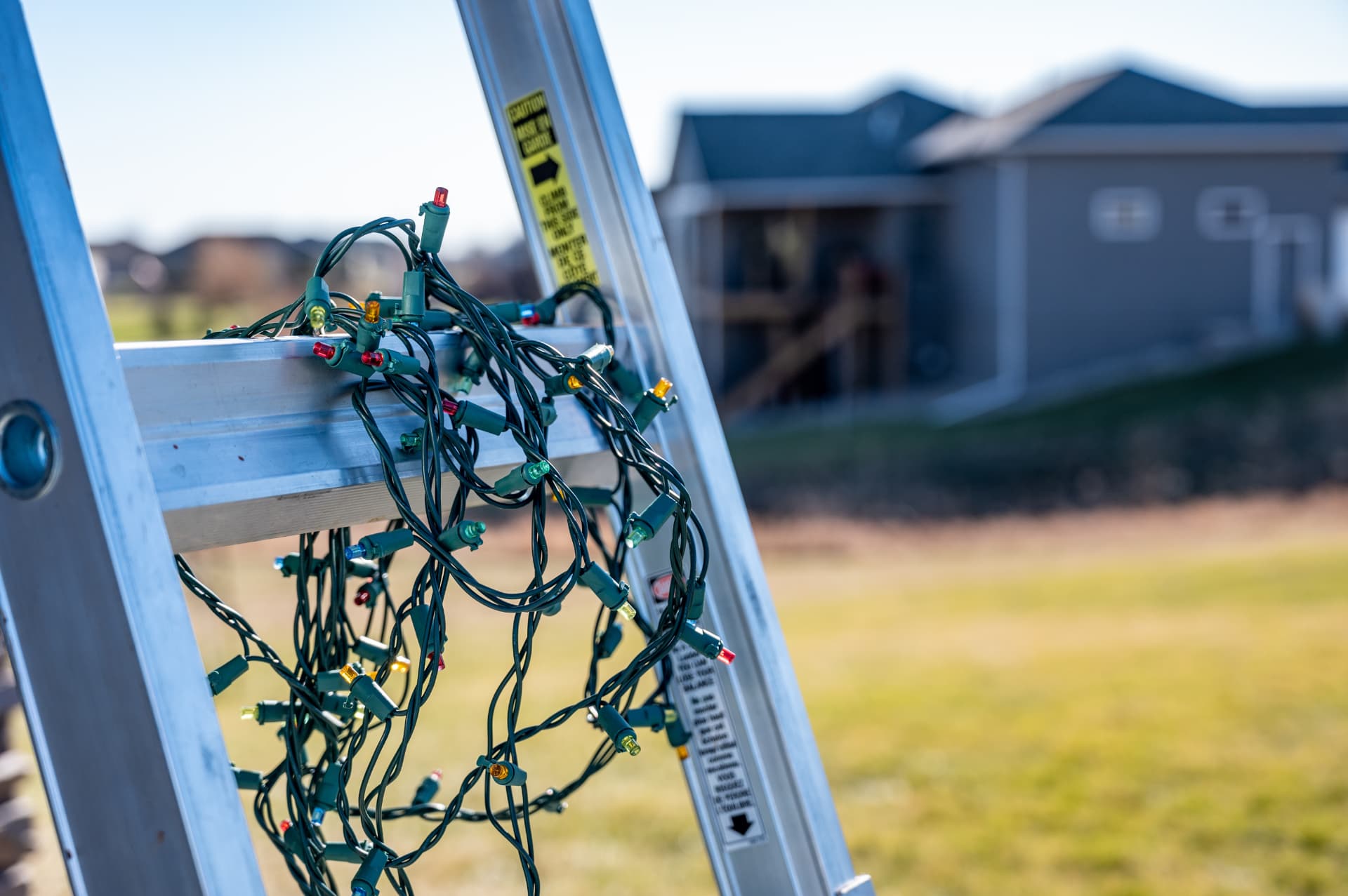 A ladder set up against a home with a strand of Christmas lights ready to hang.