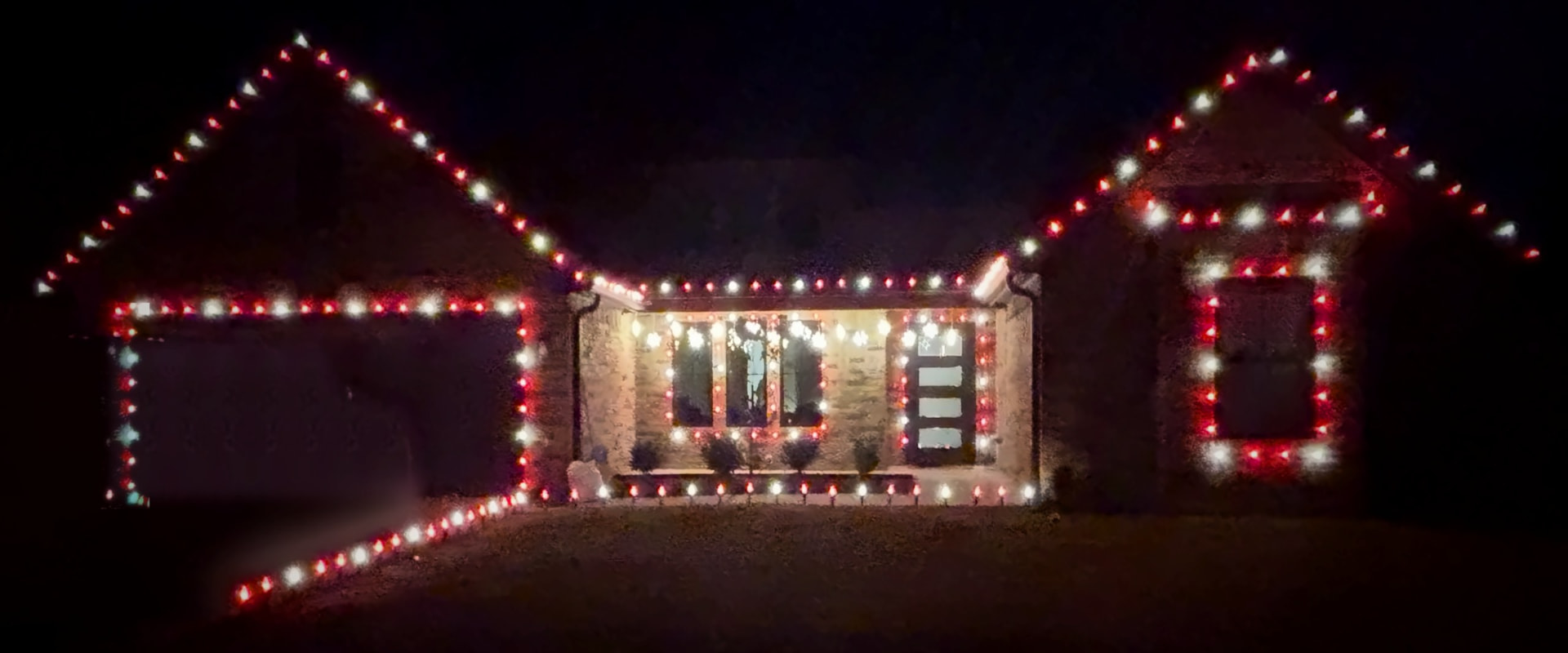 A home at night lit with red and white Christmas lights along the roofline and windows.